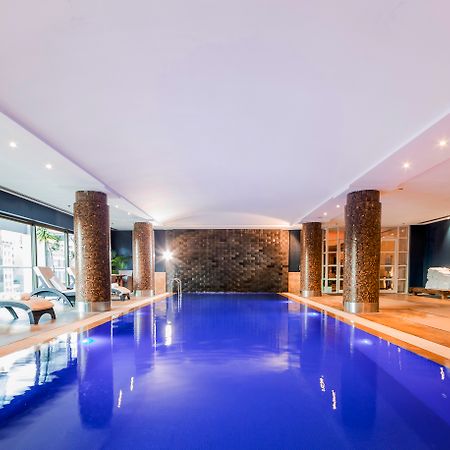 Amora Hotel Jamison Sydney Kültér fotó The photo shows an indoor swimming pool. The water is a striking blue color, and the surrounding area has modern decor. There are stone columns supporting the ceiling, and the lighting is bright and inviting. To one side, there are several lounge cha