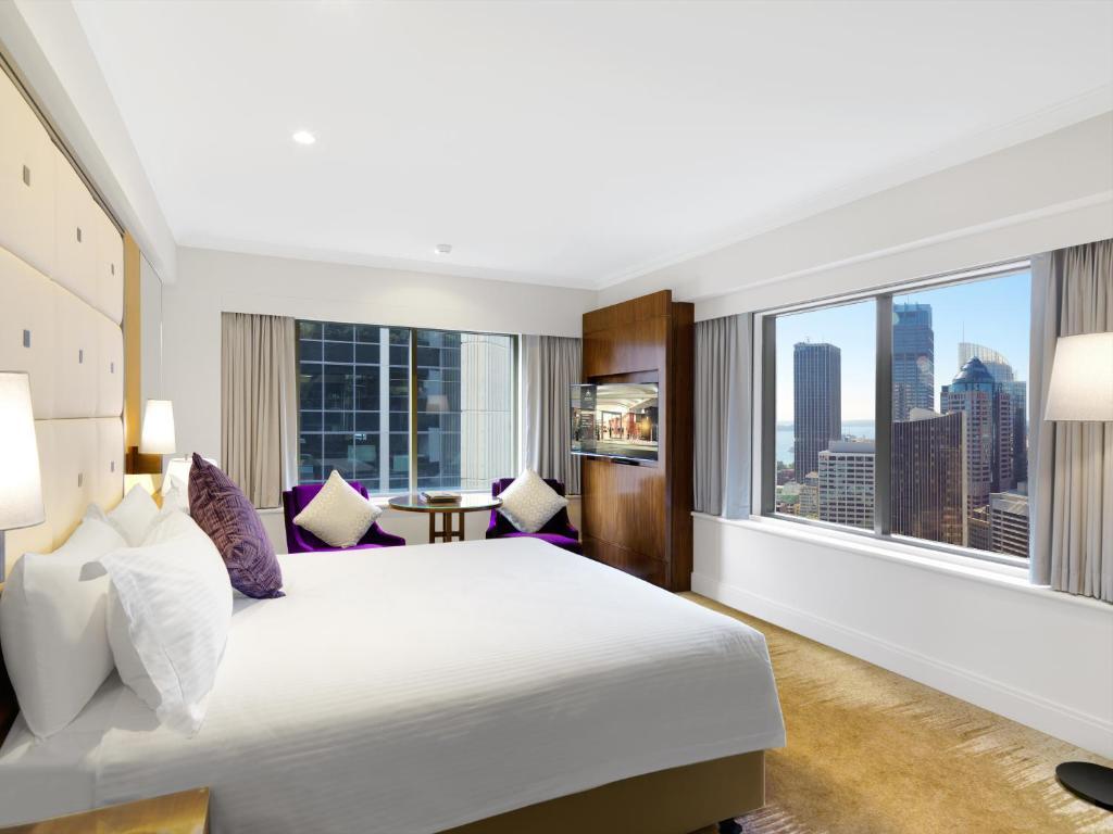Amora Hotel Jamison Sydney Kültér fotó The photo shows a modern hotel room featuring a spacious layout. There is a large bed with white bedding and purple accent pillows. The decor is minimalist and elegant, with light-colored walls and floor. To one side, there is a comfortable seating a