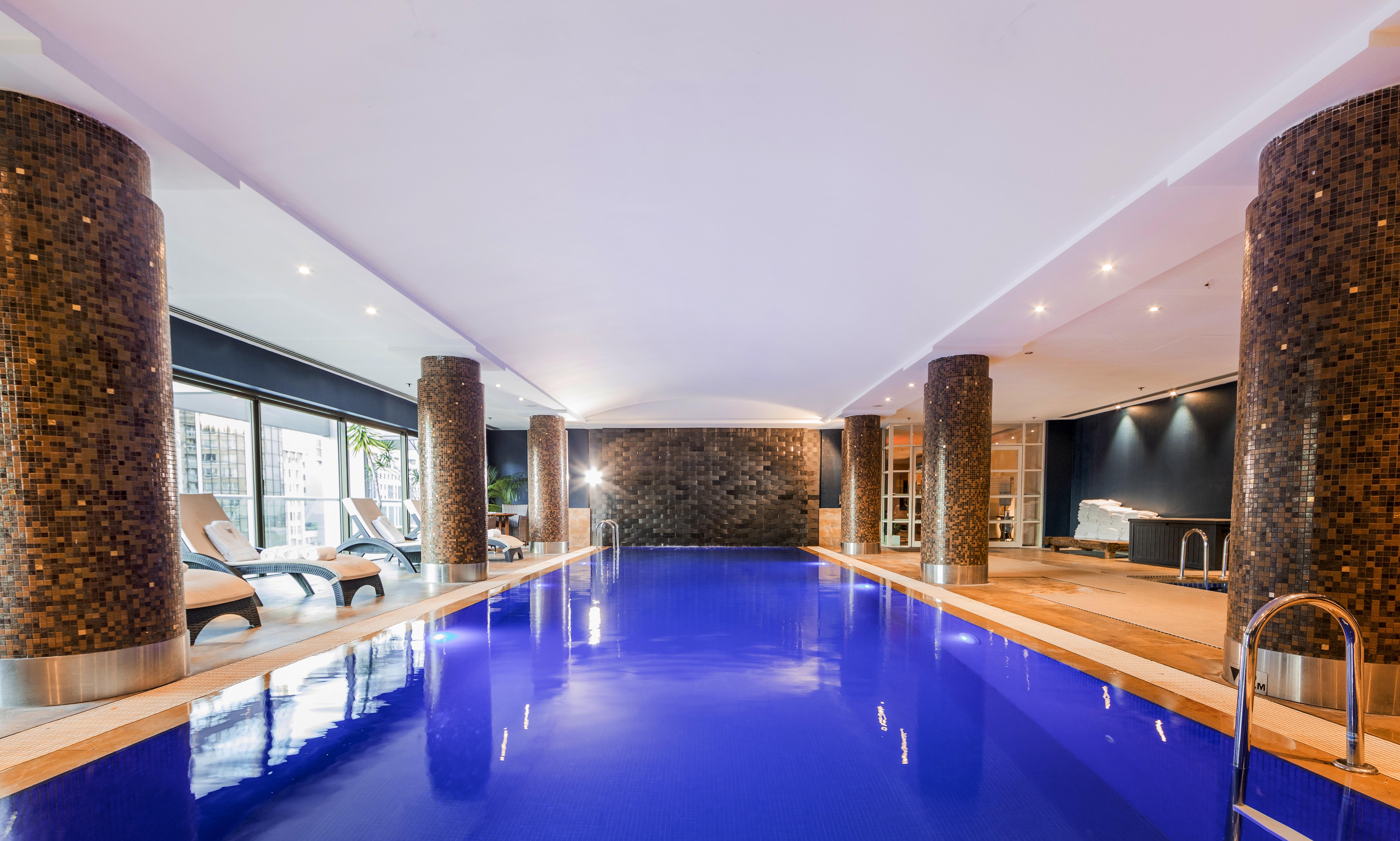 Amora Hotel Jamison Sydney Kültér fotó The photo shows an indoor swimming pool. The water is a striking blue color, and the surrounding area has modern decor. There are stone columns supporting the ceiling, and the lighting is bright and inviting. To one side, there are several lounge cha