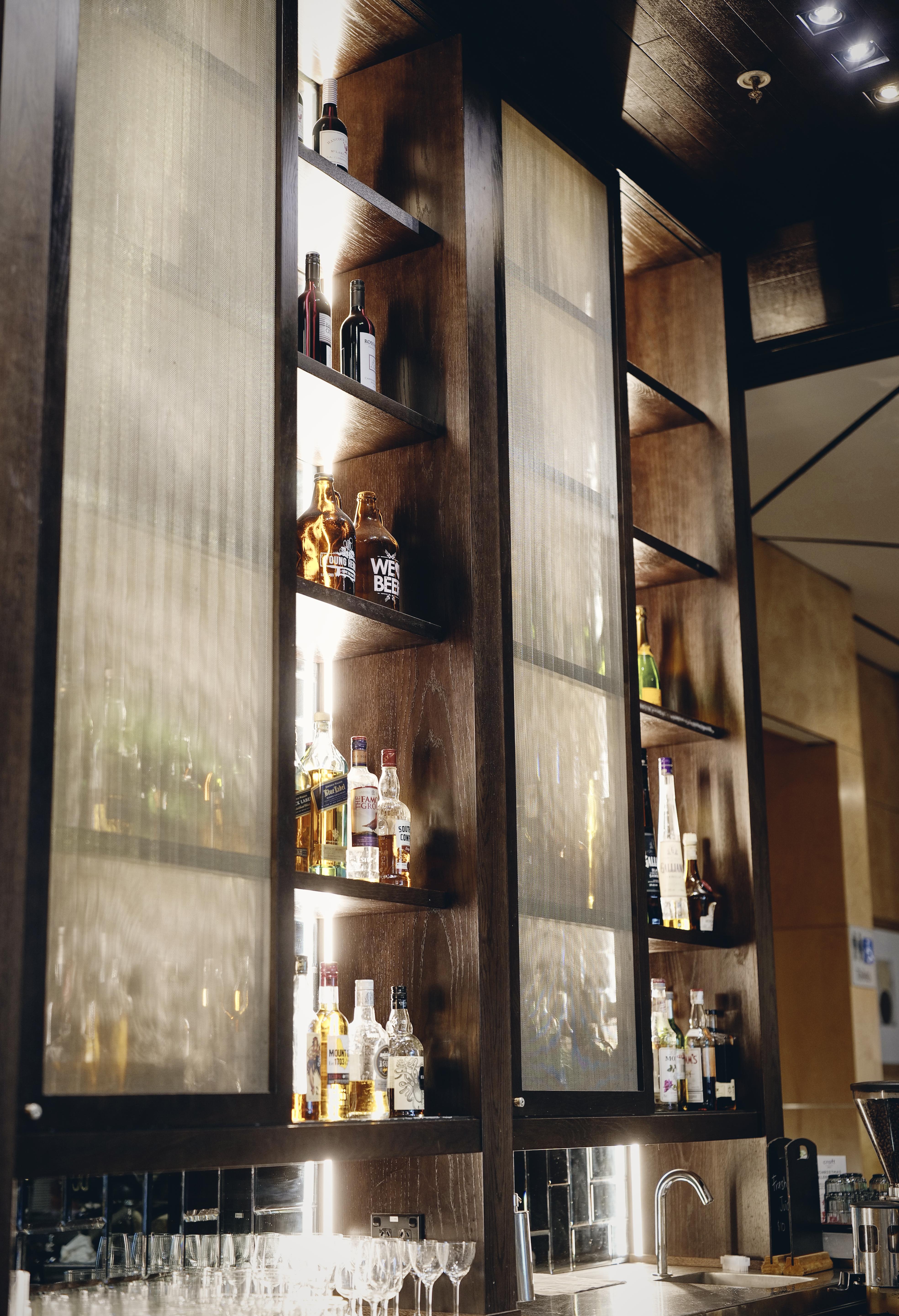 Amora Hotel Jamison Sydney Kültér fotó The photo shows a wooden shelving unit with several rows displaying various bottles of alcohol. The shelves are illuminated, highlighting the bottles, which include different types of spirits. The background has a muted tone, and the overall aestheti