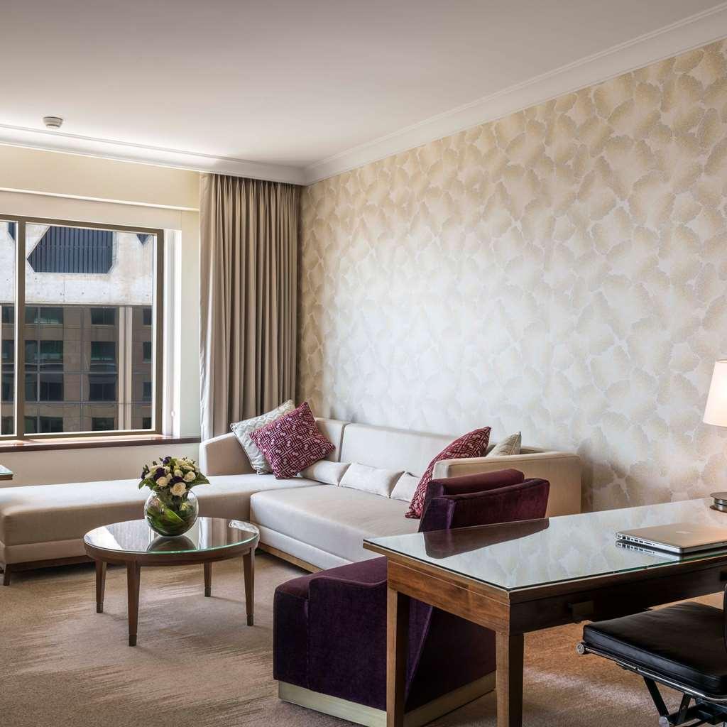 Amora Hotel Jamison Sydney Szoba fotó The photo depicts a modern and stylish living area. It features a light-colored sofa with decorative cushions, a coffee table in the center, and a desk with a chair. The walls are adorned with a patterned wallpaper, and there are large windows lettin