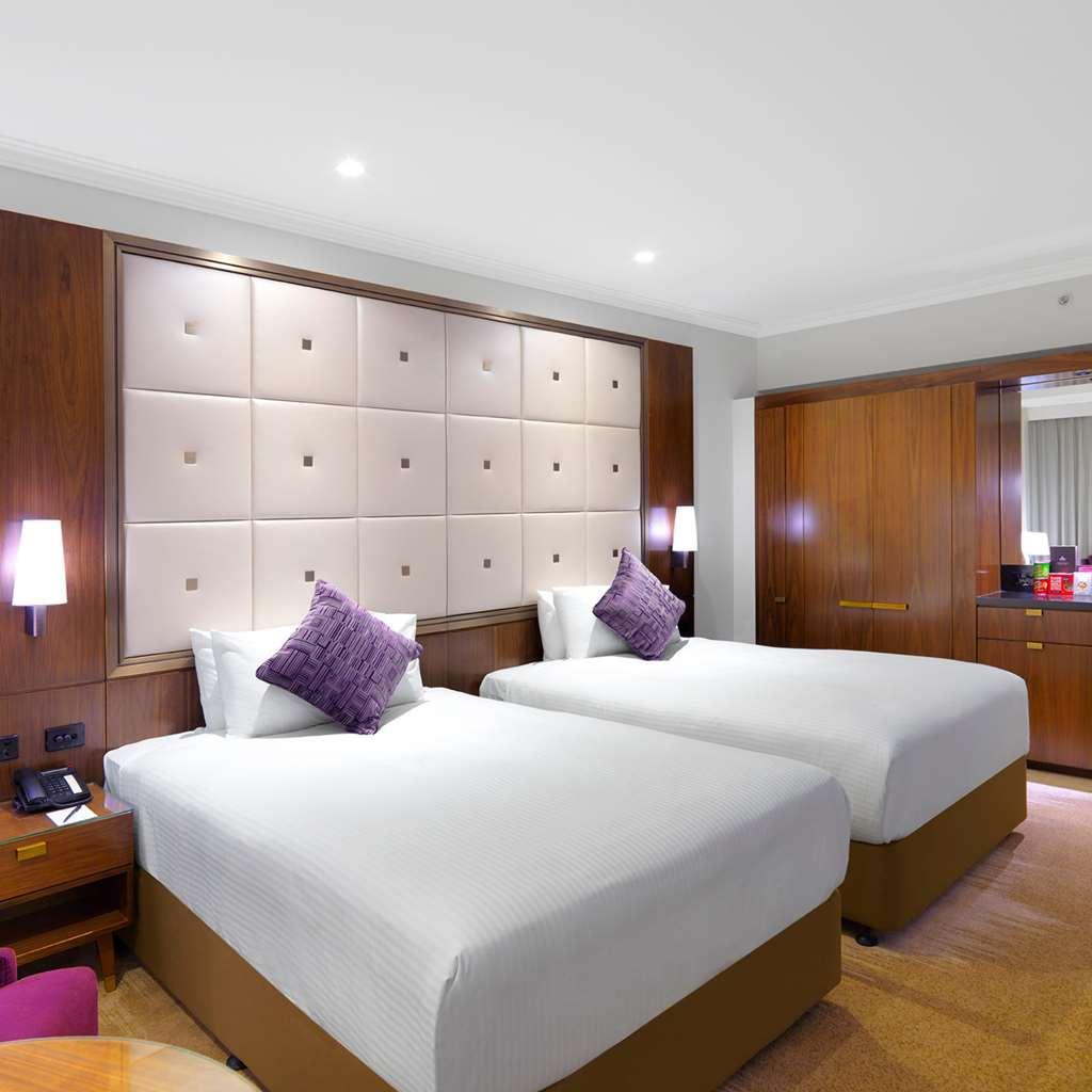 Amora Hotel Jamison Sydney Szoba fotó The photo depicts a hotel room featuring two twin beds with white beddings. Each bed is accented by a purple decorative pillow. The room has a modern design, with a large upholstered headboard that has a grid pattern. There are warm wooden elements i