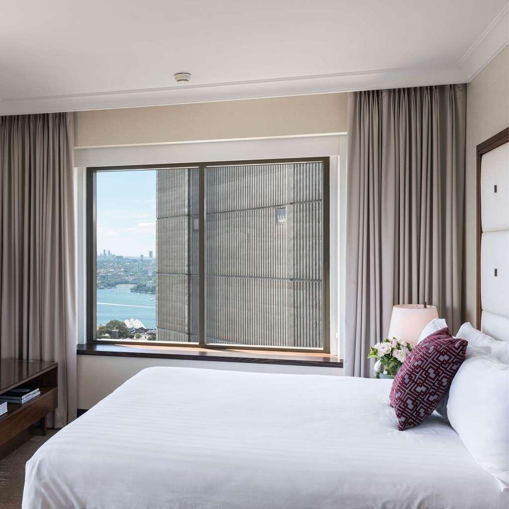 Amora Hotel Jamison Sydney Szoba fotó The photo shows a modern hotel room with a large window that offers a view of the outside. The room features a neatly made bed with white bedding and a decorative pillow. There are light-colored curtains framing the window, which appears to overlook 