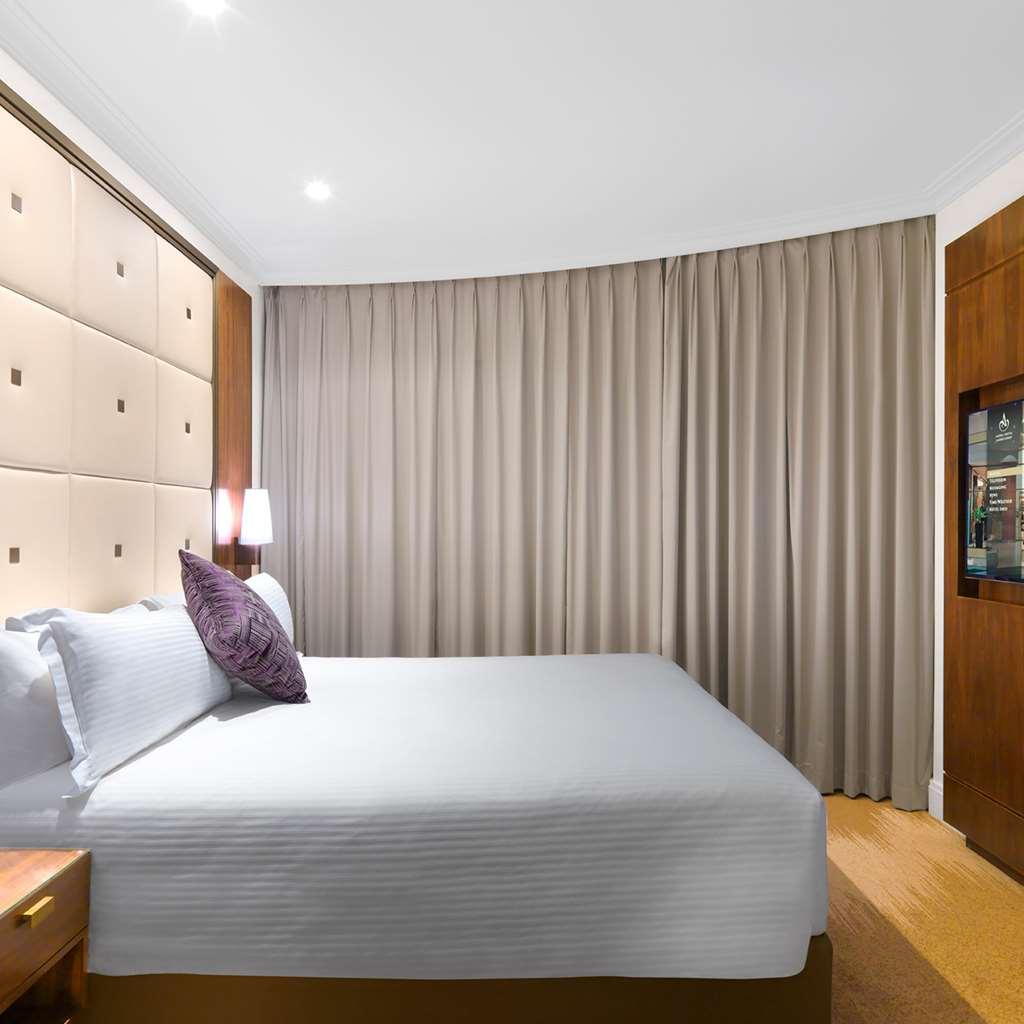 Amora Hotel Jamison Sydney Szoba fotó The photo shows a modern hotel room with a neatly made bed featuring light-colored bedding and a decorative pillow. The headboard behind the bed has a soft, upholstered design with square patterns. To the right, there is a wooden cabinet, and on the 