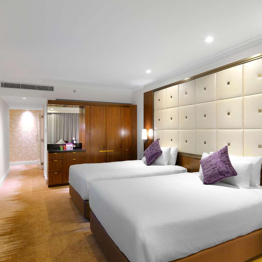 Amora Hotel Jamison Sydney Szoba fotó The photo shows a modern hotel room featuring two twin beds with white bedding and purple decorative pillows. The walls are designed with soft beige panels, creating a luxurious ambiance. There’s wooden furniture, including a cabinet against one wall