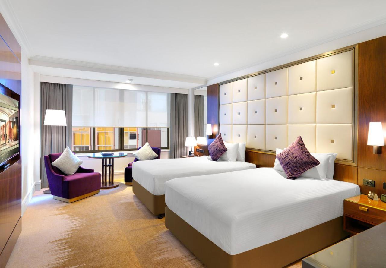 Amora Hotel Jamison Sydney Kültér fotó The photo shows an elegant hotel room featuring two beds with white linens and decorative pillows. The beds are positioned against a stylish headboard with a soft, padded design. There’s a cozy seating area with a purple armchair and a small round ta