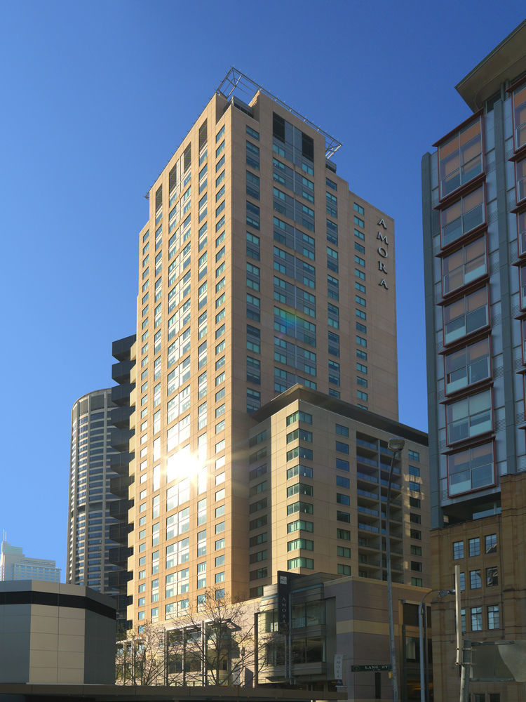 Amora Hotel Jamison Sydney Kültér fotó The photo shows a tall building with a modern architectural design, featuring a mix of glass and concrete materials. The building is predominantly light-colored with large windows reflecting sunlight. It appears to have multiple floors, and the name 