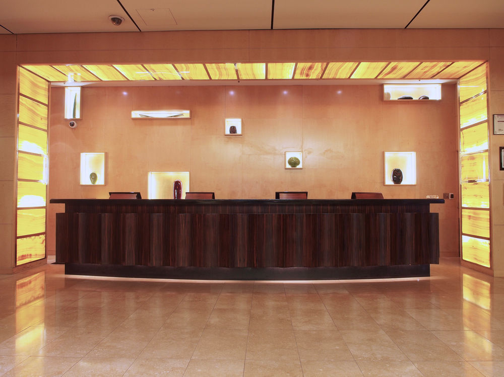 Amora Hotel Jamison Sydney Kültér fotó The photo shows a modern reception area. At the center is a sleek, dark wood reception desk. Behind the desk, there is a wall that features illuminated sections in warm tones, creating an inviting atmosphere. There are several small display niches in