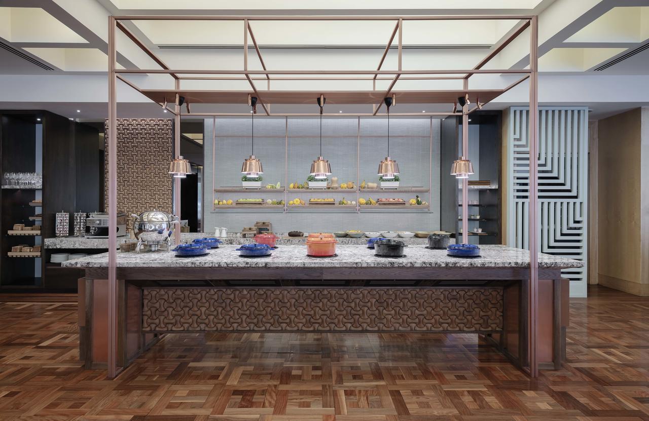 Amora Hotel Jamison Sydney Kültér fotó The photo shows a modern dining area, likely a buffet setup. There is a long table made of wood and marble, featuring multiple food display options. Above the table, there are hanging light fixtures. The background includes a wall with shelves displa