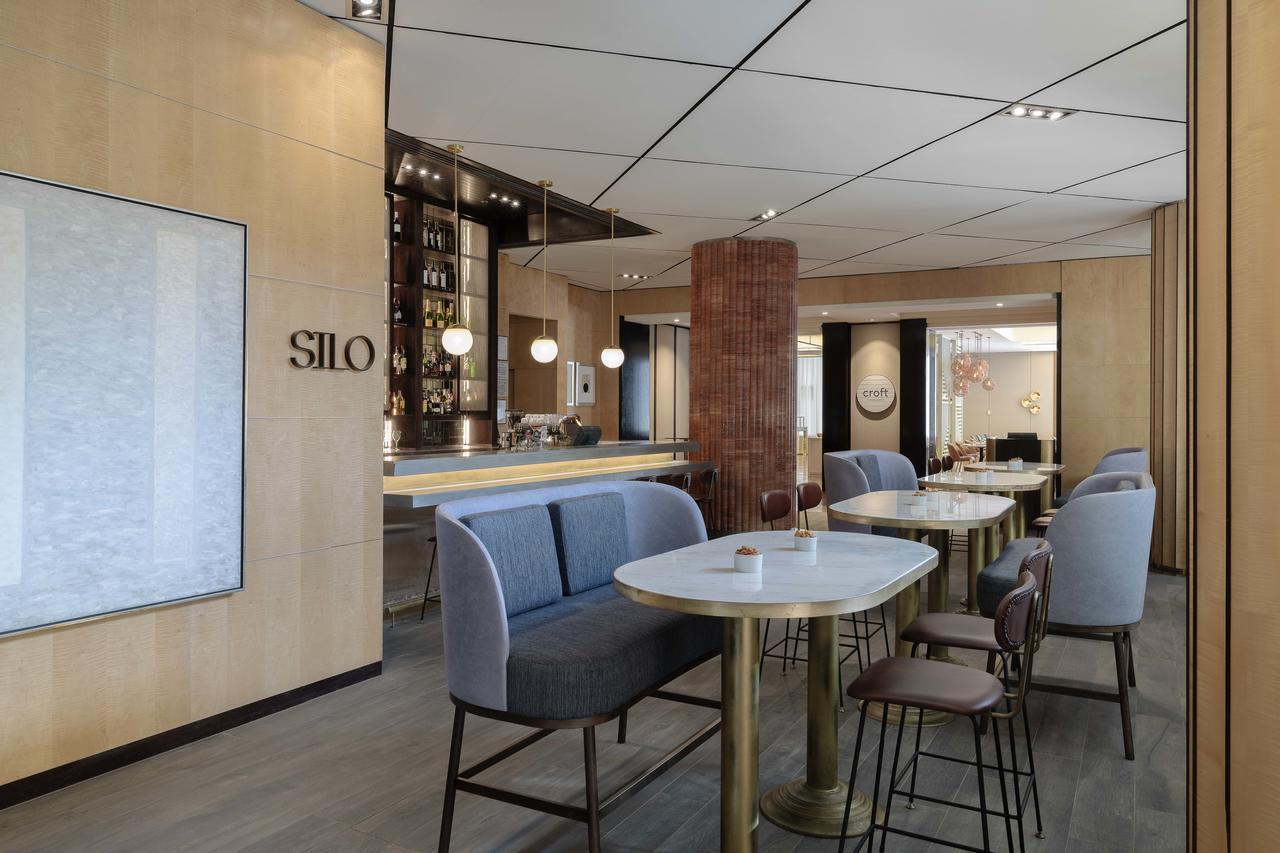 Amora Hotel Jamison Sydney Kültér fotó The photo shows a modern and stylish interior of a space called "SILO." It features a combination of seating options, including high chairs and low tables with a sleek design. The decor has a warm, inviting atmosphere with wooden paneling and soft li