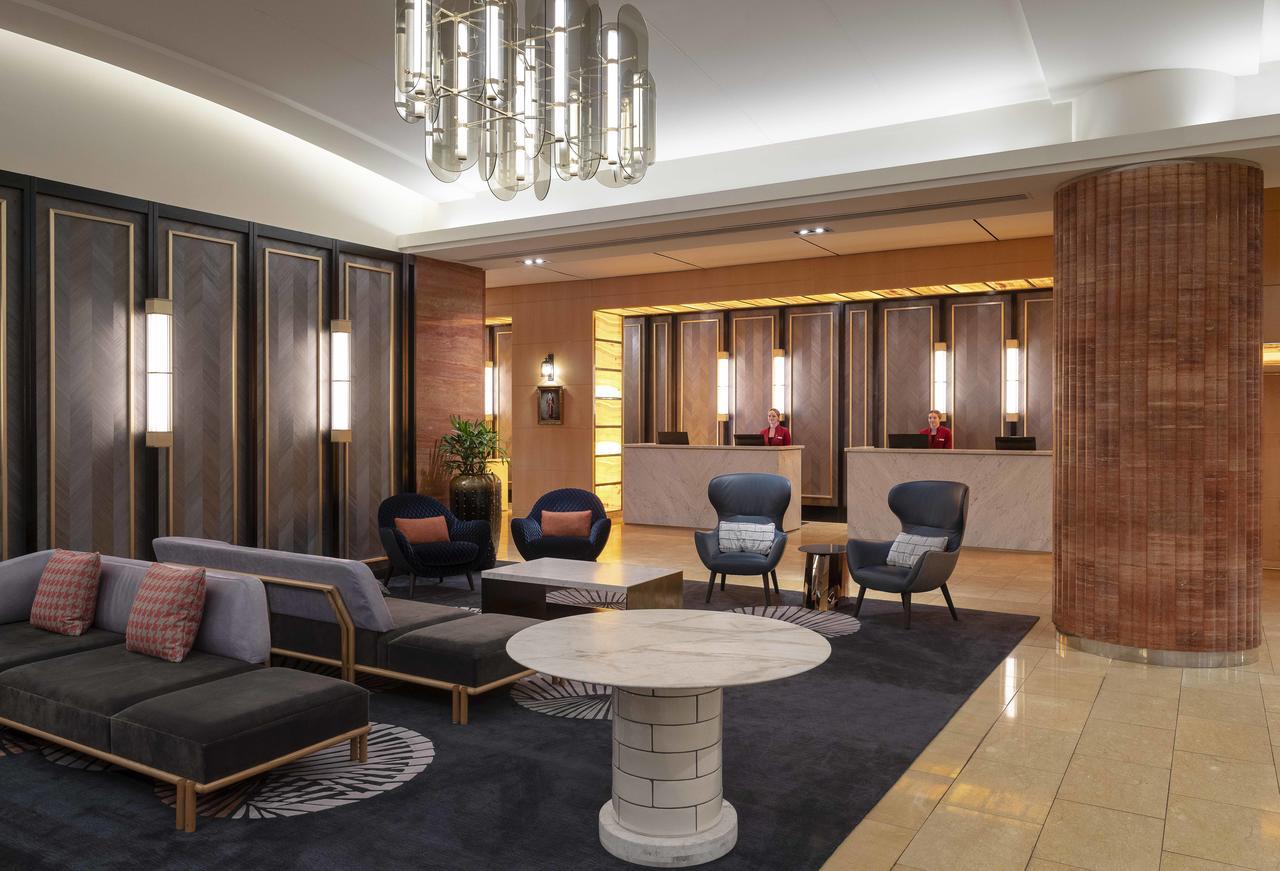 Amora Hotel Jamison Sydney Kültér fotó The photo depicts a modern hotel lobby. It features stylish furniture, including a black and gray seating area with cushions, and two blue accent chairs. A round, white coffee table sits in the center of the seating arrangement. The background shows 