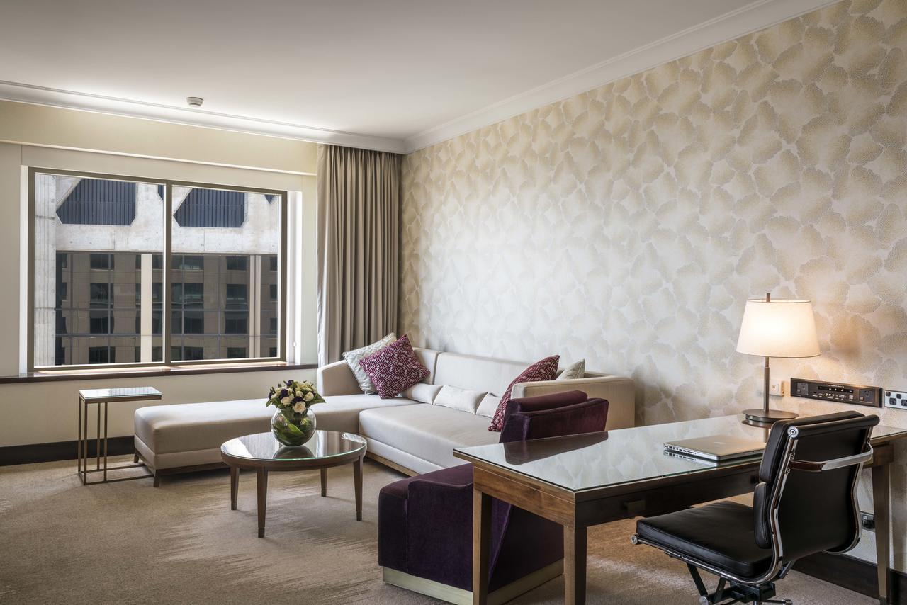 Amora Hotel Jamison Sydney Kültér fotó The photo shows a modern hotel room or a stylish living area. There is a comfortable white sofa with decorative pillows arranged in a cozy seating area. A glass coffee table with a small floral arrangement is positioned in front of the sofa. To the r