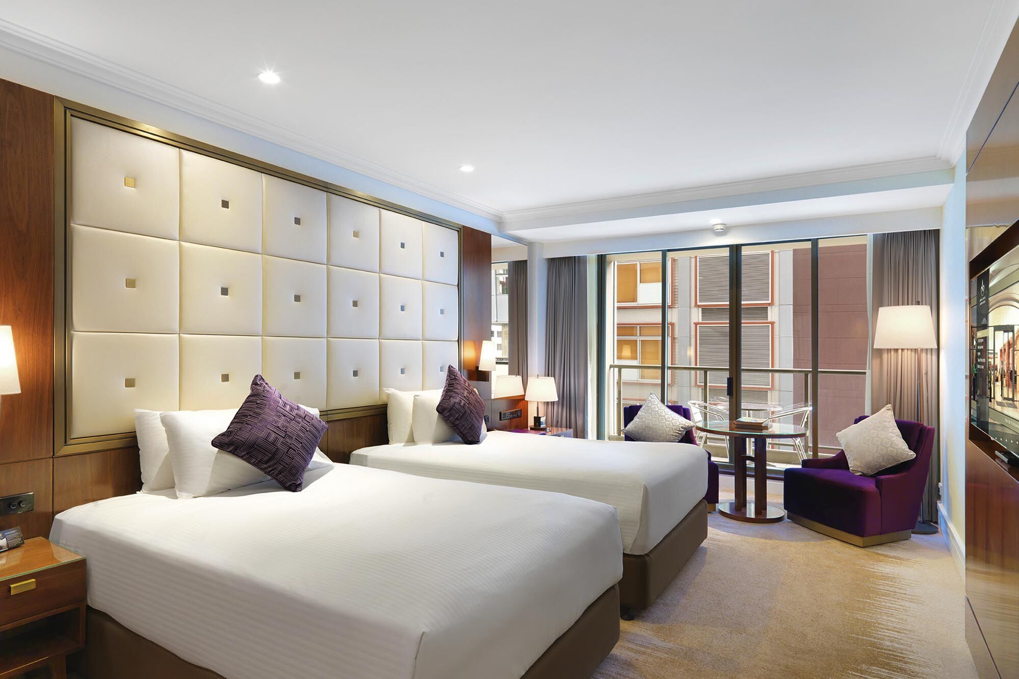 Amora Hotel Jamison Sydney Kültér fotó The photo depicts a modern hotel room featuring two neatly made beds with white linens and purple accent pillows. The walls are partially covered with a padded paneling, creating an elegant backdrop. There is a large window with sheer curtains allowi