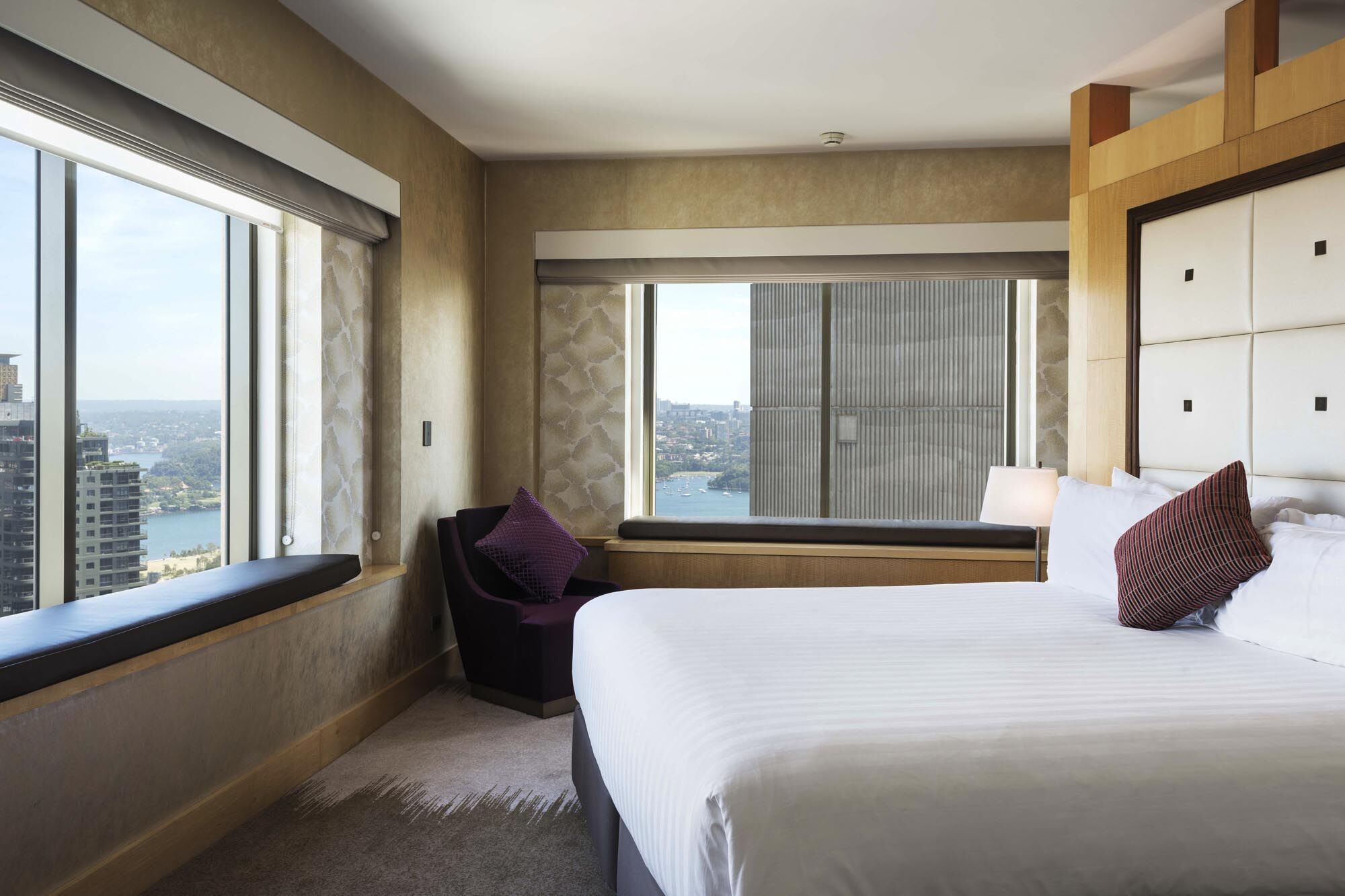 Amora Hotel Jamison Sydney Kültér fotó The photo shows a modern, stylish hotel room featuring a bed with white linens, a decorative pillow, and a cozy chair with a purple cushion. Large windows provide a view of the outside scenery, which appears to include a body of water and buildings. 