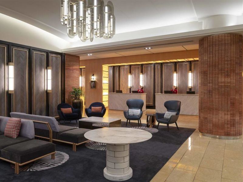 Amora Hotel Jamison Sydney Kültér fotó The photo depicts a stylish hotel lobby. There are several modern seating arrangements featuring dark upholstered couches and armchairs placed around a round marble coffee table. The design incorporates a combination of elegant lighting fixtures and 