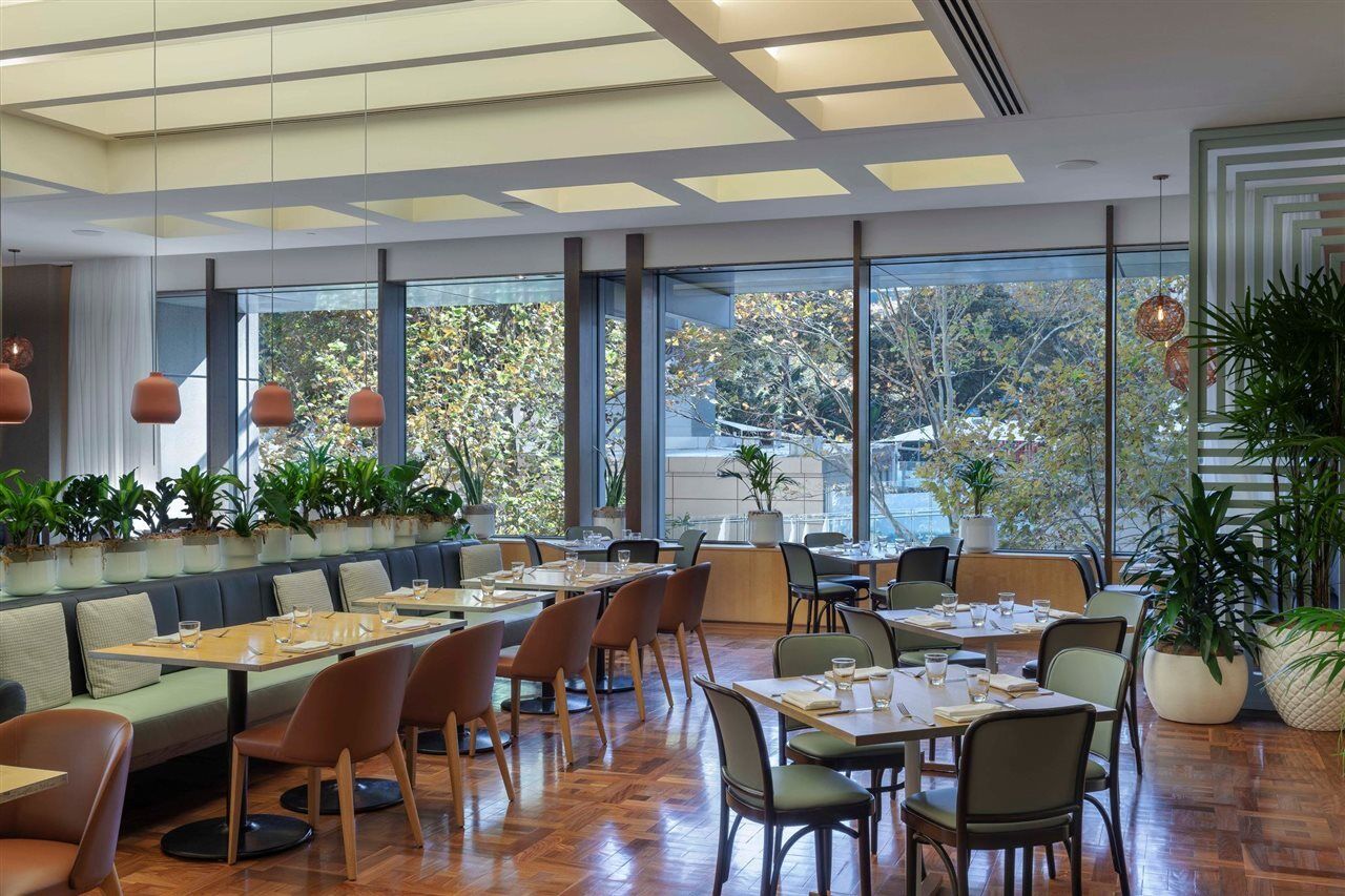 Amora Hotel Jamison Sydney Kültér fotó The photo shows a modern restaurant interior characterized by a spacious layout with large windows allowing natural light to fill the room. There are several dining tables arranged throughout the space, some set for meals with dishes and utensils, wh